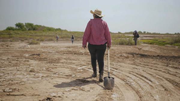 A photograph of a woman dragging a shovel through a field