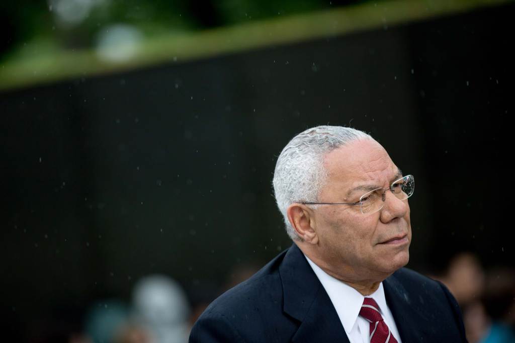 Colin Powell wearing a dark suit looks onward–his glasses catching raindrops.
