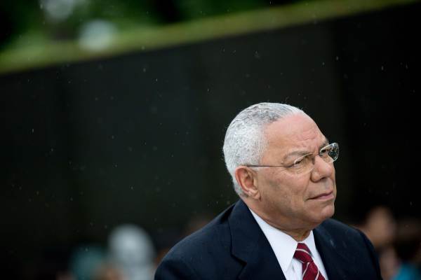  Colin Powell wearing a dark suit looks onward–his glasses catching raindrops.