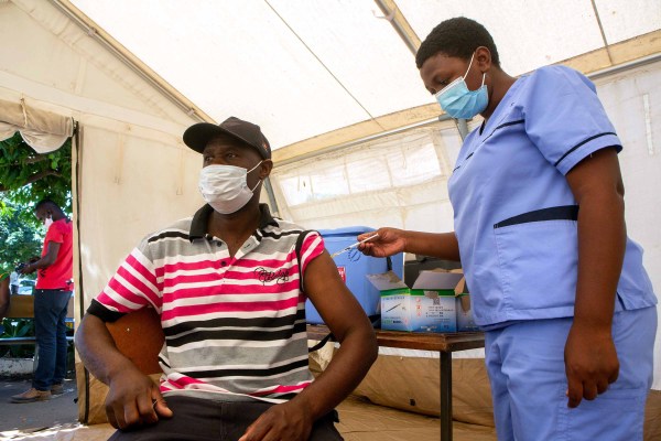 A nurse in light blue scrubs administers a Covid 19 vaccine to a man wearing a mask inside a tent at Harare, Zimbabwe