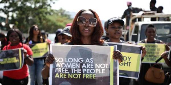 A Black woman, surrounded by fellow demonstrators, holds a sign that reads "So long as women are not free, the people are not free" near the Federal Capital Territory in Abuja, Nigeria.