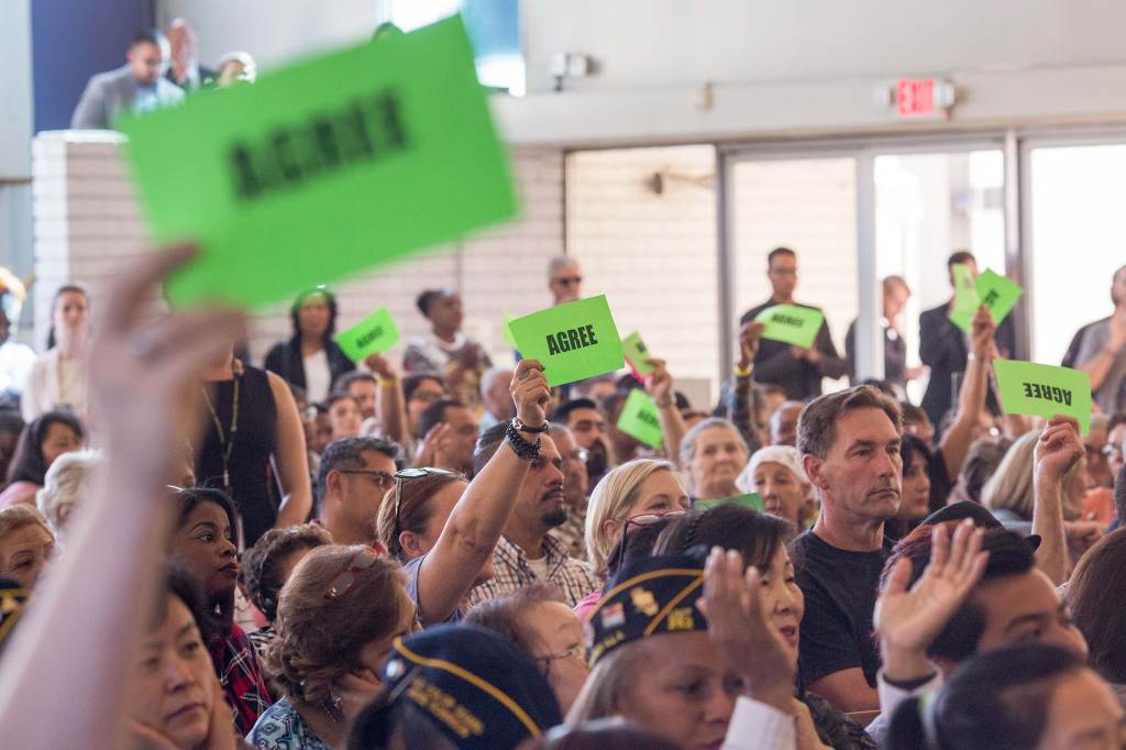 A crowd at a town hall holding up green sights that read “Agree.”