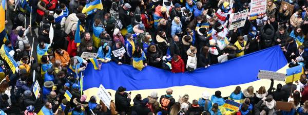 A dense crowd of demonstrators dressed in yellow and blue unfurling a large Ukrainian flag.