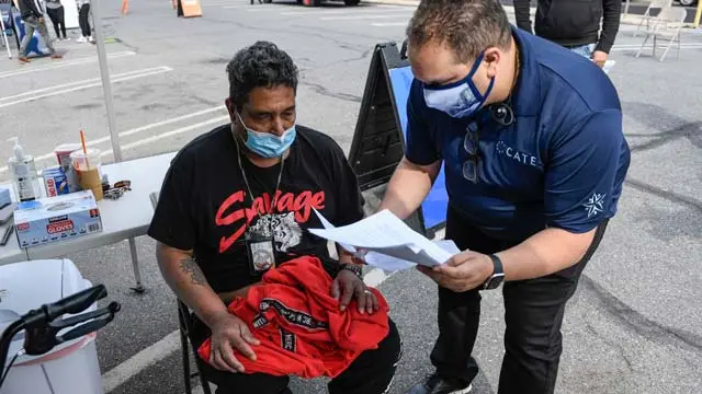 George Fernandez (wearing a navy polo shirt and black pants), the Founder and CEO of Latino Connection, talk with a patient wearing black shirt and black pants, seated, who is waiting to get his COVID-19 vaccine.