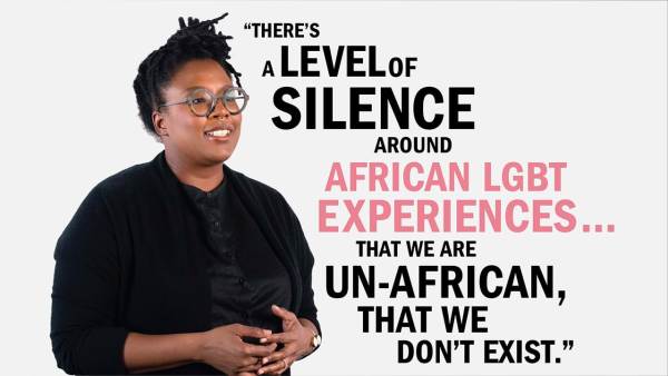 Selly Thiam has black dreads tied up in a knot and is wearing dark thick-rimmed eyeglasses. She has a nose ring and wears a black sweater over a black blouse. She's standing next to copy that reads, "There's a level of silence around African LGBT experiences... that we are Un-African, that we don't exist."