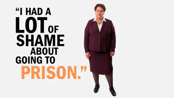 Vivian Nixon has short brown curly hair wearing wire-rimmed glasses and a burgundy blazer and skirt over a white collared blouse. She's standing next to copy that reads, "I had a lot of shame about going to prison."