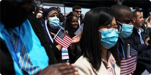 Diverse group of people wearing blue surgical masks and holding small American flags.