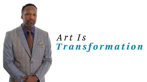Carlton Turner, a black man, is wearing a gray striped suit, a dark blue button-down shirt, and a brown tie with light dots. The phrase "Art Is Transformation" appears to his right.