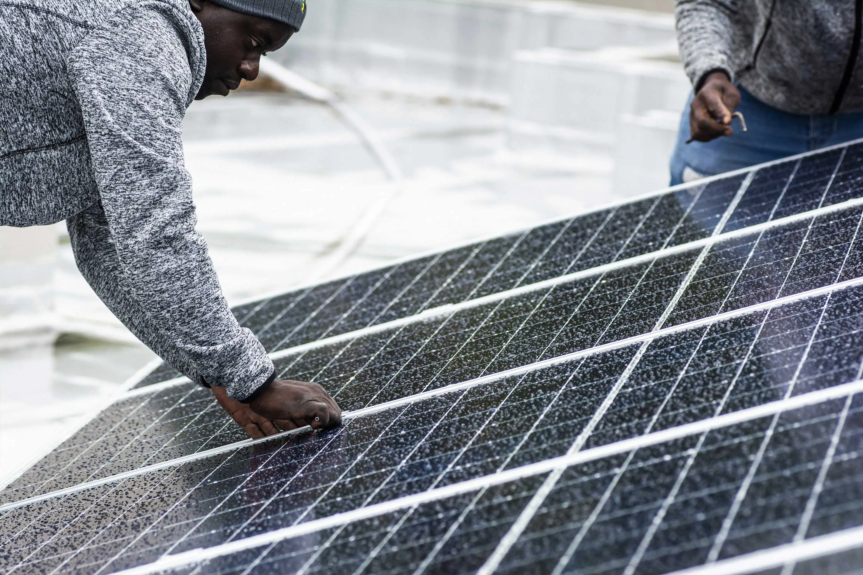 A Black worker  wearing a gray sweatshirt and dark gray beanie installing  a solar panel. 