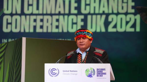  Tuntiak Katan,a member of the Shuar people, General Coordinator of the Indigenous Organizations of the Amazon Basin (COICA) speaking at the UN Climate Change Conference UK 2021. He is wearing a traditional head garment and a suit with traditional patterns draped across it.