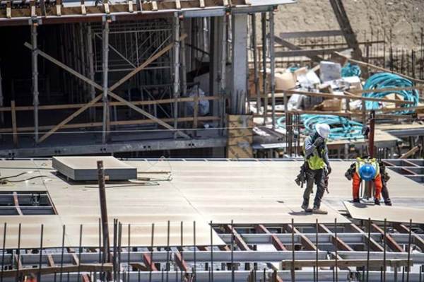 An aerial view of a construction site with two workers on the top level laying down some plywood.