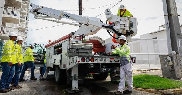 Emergency workers wearing bright yellow shirts prepare to work on downed power lines besides a truck in in Puerto Rico.
