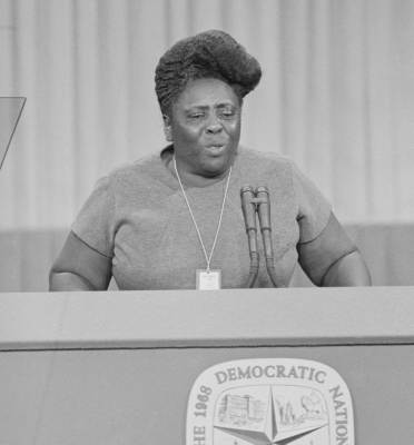 Fannie Lou Hammer, a Black woman with an updo speaks at a podium on stage.