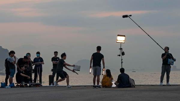 Group of Asian film staff on set filming in the evening along a shoreline in Hong Kong, China.