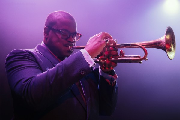Image of a bald man wearing glasses playing a trumpet.