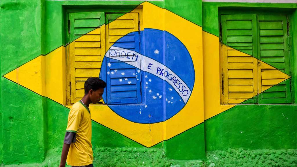 A person wearing a yellow jersey walks past a mural of the Brazilian flag.