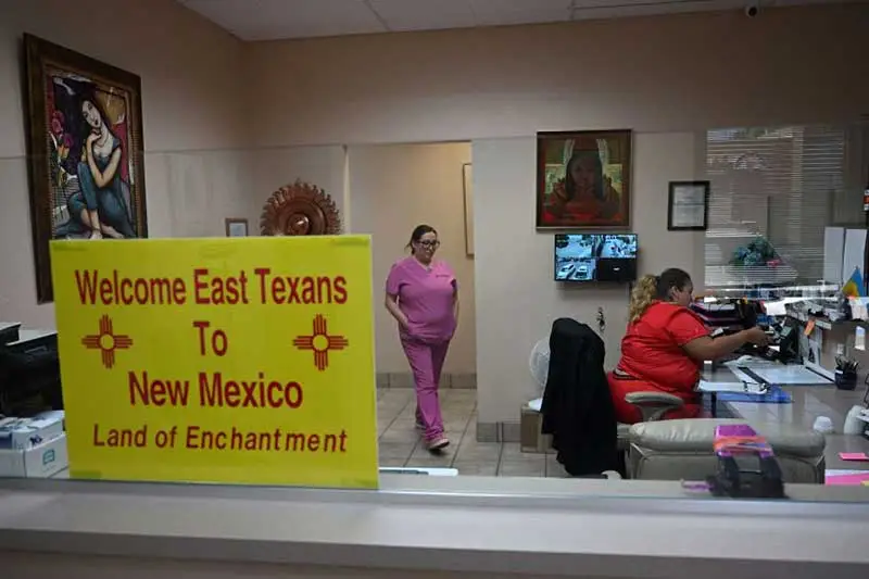 A sign welcoming patients from East Texas is displayed in the waiting area of the Women's Reproductive Clinic in Santa Teresa, New Mexico. In the background there are two nurses attending the welcome desk.