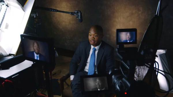 Fred Swaniker sitting on a film set in front of multiple cameras with his face displayed on all monitors. 