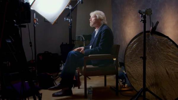 Richard Branson sitting on a film set lit with a bright white light. 