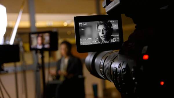 Risa Lavizzo-Mourey on a film set in front of cameras with her face on multiple monitors. 