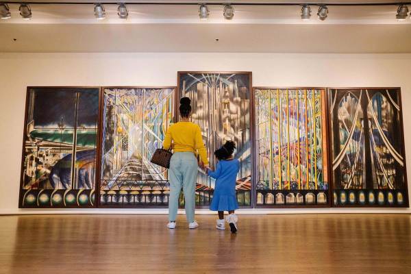 A woman and child stand before a five-paneled painting in a gallery. The panels each depict abstract scenes of bridges in fantastical colors.