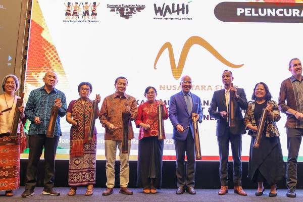 Representatives from the Ford Foundation and Indonesian NGOs smile and hold traditional musical instruments on stage. Behind them is an illuminated screen with the logos of the various organizations.