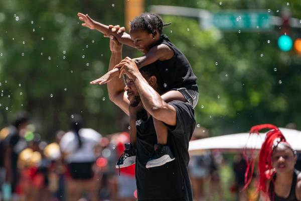 A Black man and a Blaack child enjoy bubbles blown by a spectator while marching in the Juneteenth Atlanta Black History parade.
