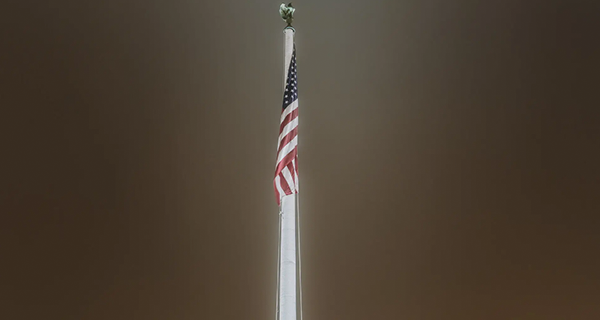 Night-time picture of an American Flag hanging from a flag pole.