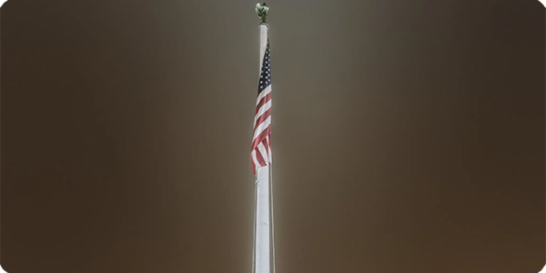 Night-time picture of an American Flag hanging from a flag pole.