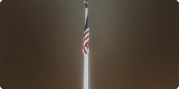 Night-time picture of an American Flag hanging from a flag pole.