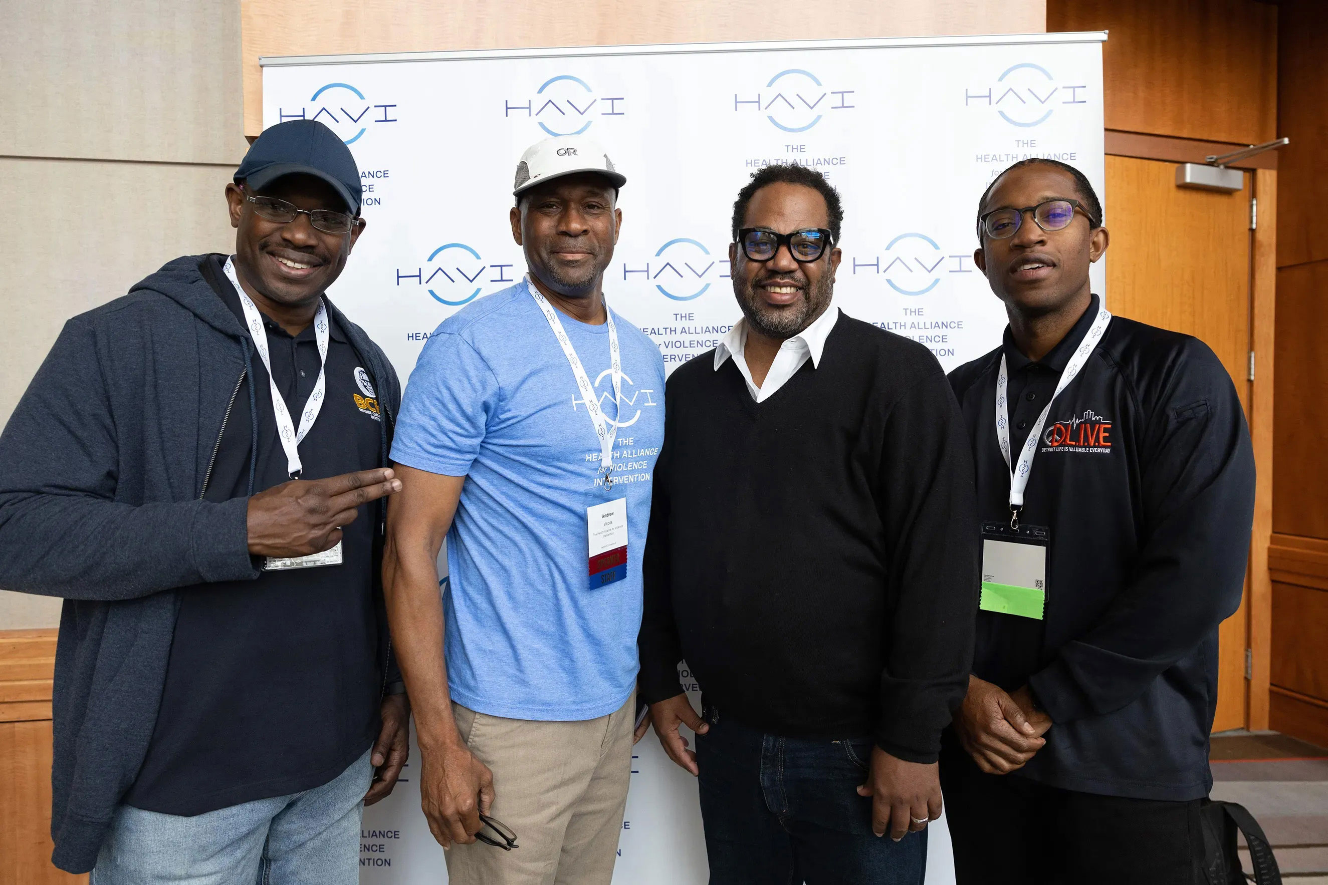 Four men stand together in front of a white backdrop featuring the "HAVI: The Health Alliance for Violence Intervention" logo. They are dressed in casual professional attire and wearing conference lanyards. This image represents community health leadership, professional networking, and violence intervention advocacy.