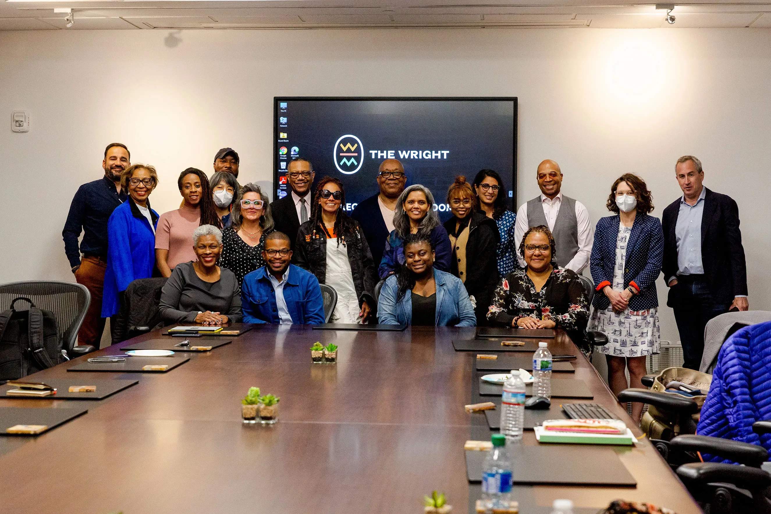 A group of smiling people sitting at the end of a conference table. Behind them is a sign for the Wright Museum