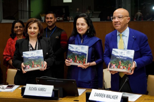 Three individuals holding copies of a book titled "हम | When Women Lead" at a un event, with name tags in view, inside a conference room.