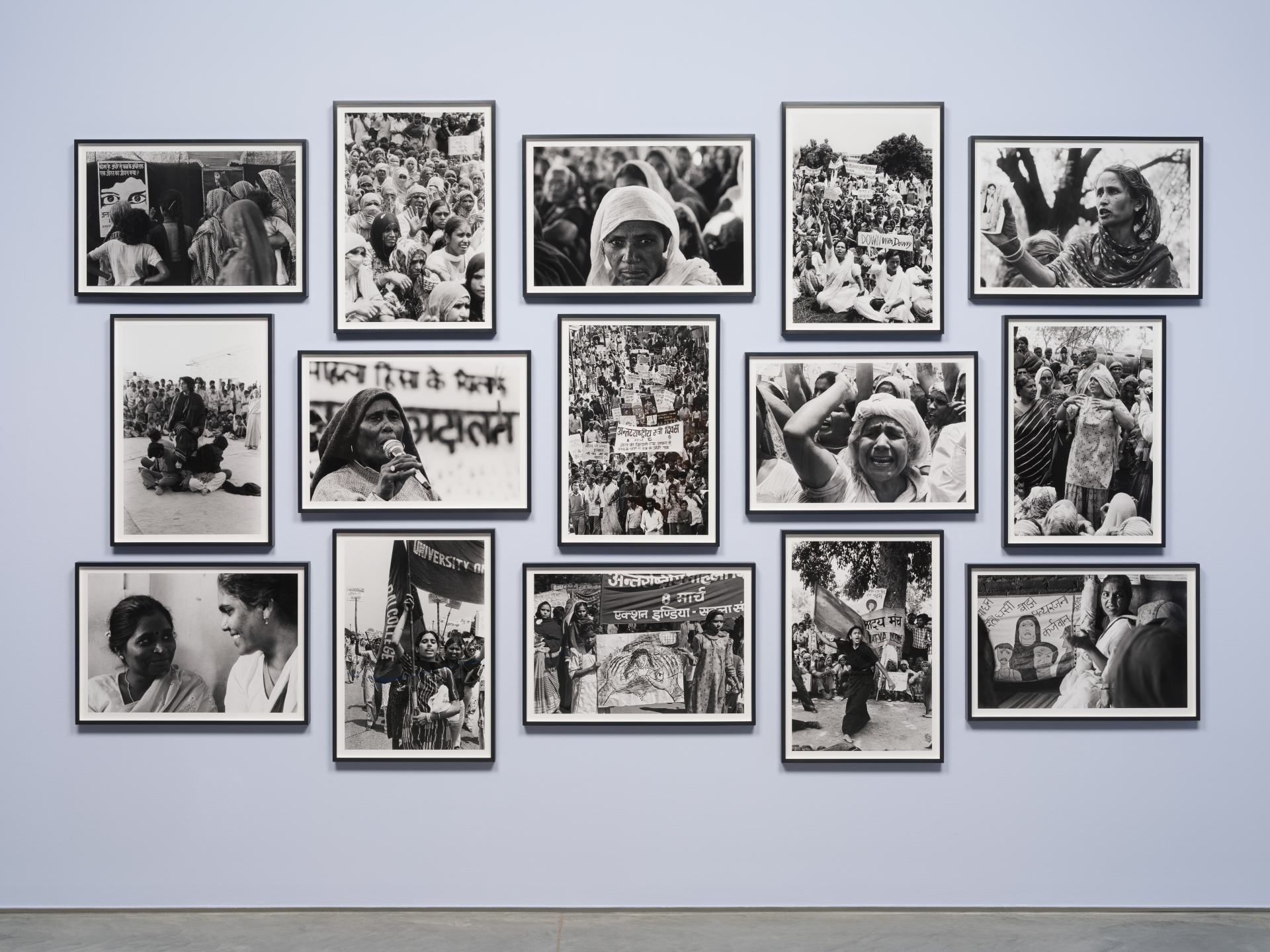 Fifteen framed black and white photographs arranged on a light lavender wall.