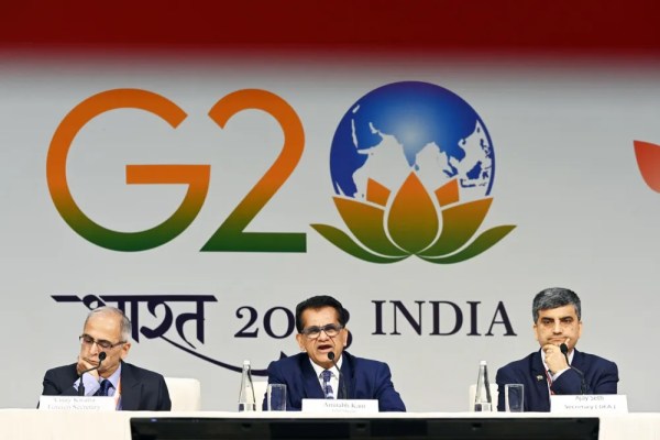 Three men sitting at a conference table with a backdrop displaying the logo "g20 india 2023" and a lotus symbol.