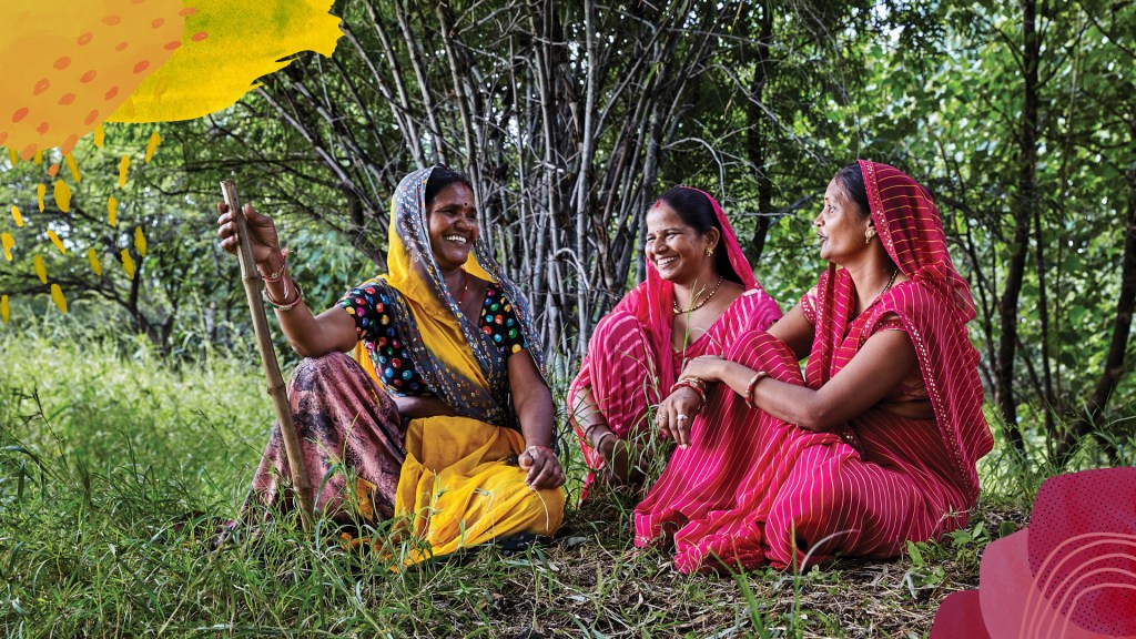 Three women in traditional Indian attire sit joyfully in a lush green garden under a colorful, artistic sun and flower overlay.