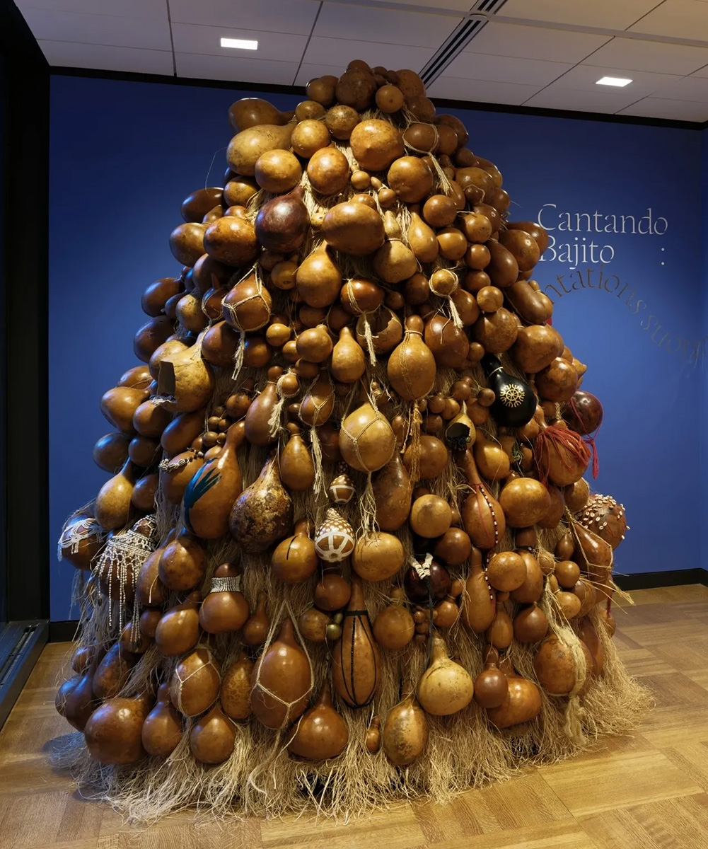 A large sculpture made up of piled gourds and straw positioned in the center of a gallery.