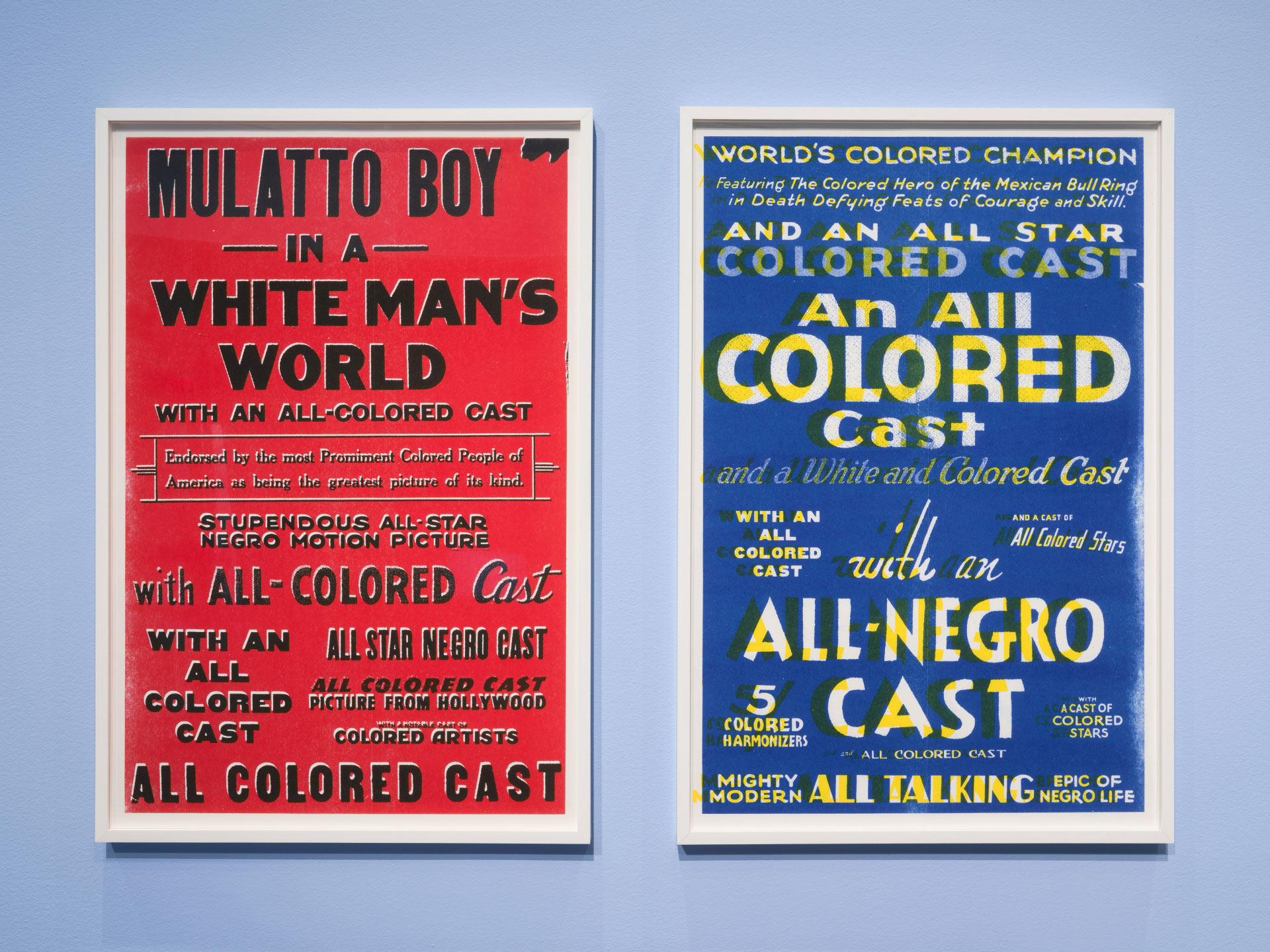One red and one blue framed posters on a light blue gallery wall.