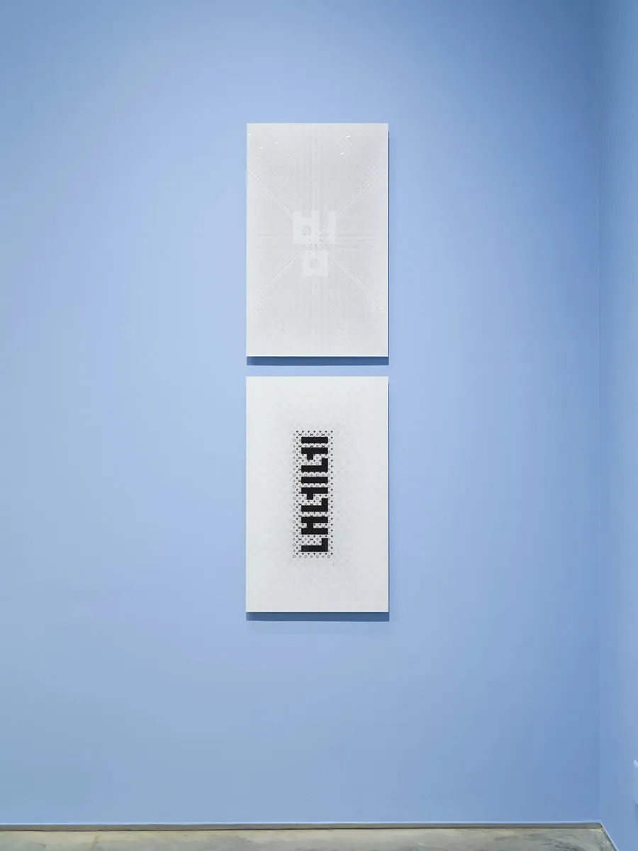 Two white vertical prints with Korean characters overlaid against a Louis Vuitton pattern hanging on a light blue wall.