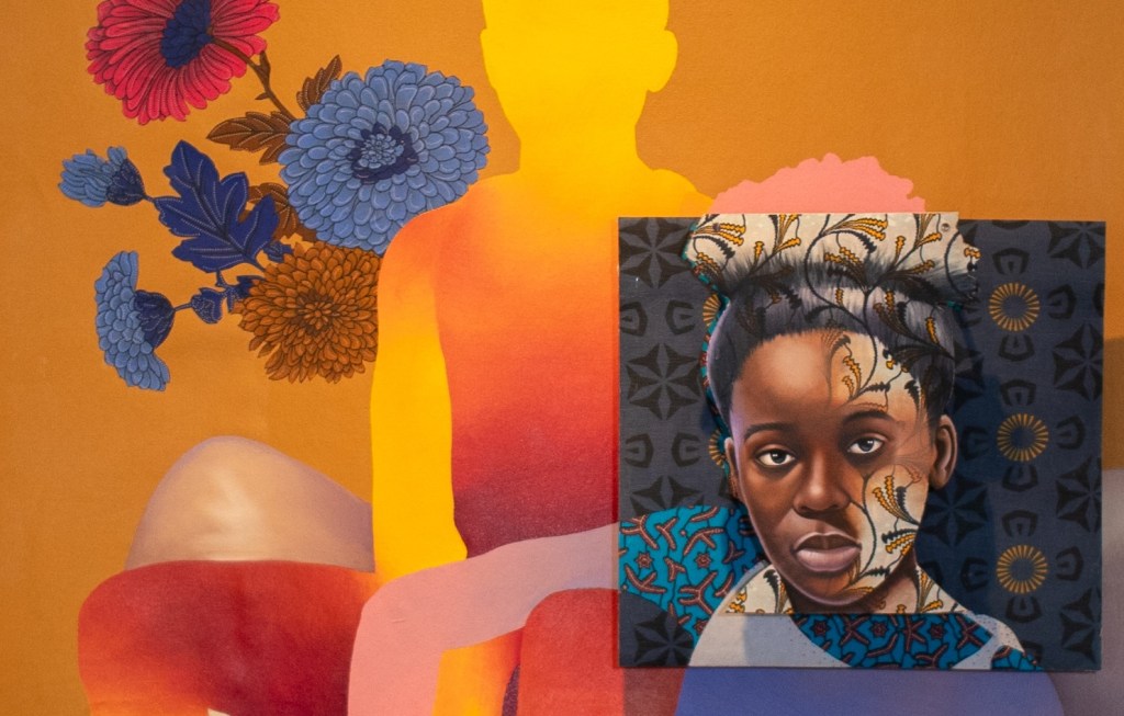 A vibrant artwork shows a portrait of a Black woman layered with patterns on her head set over a painted silhouette of a seated figure, surrounded by colorful flowers on an orange, red, and yellow background.