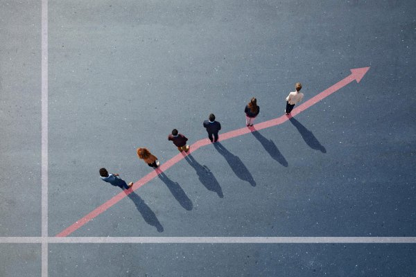 Five people are standing on a gray surface, each positioned at different points along a rising red arrow, symbolizing growth or progress, with long shadows cast behind them.