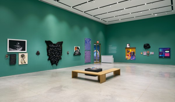 A green gallery interior with artworks of various mediums including canvas, photography, sculpture and mixed media.