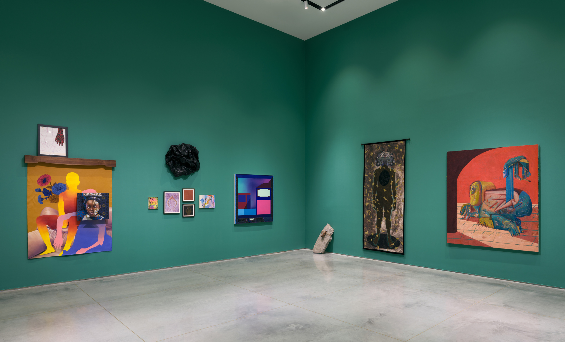 A corner of a gallery exhibiting various artworks against a green painted wall.