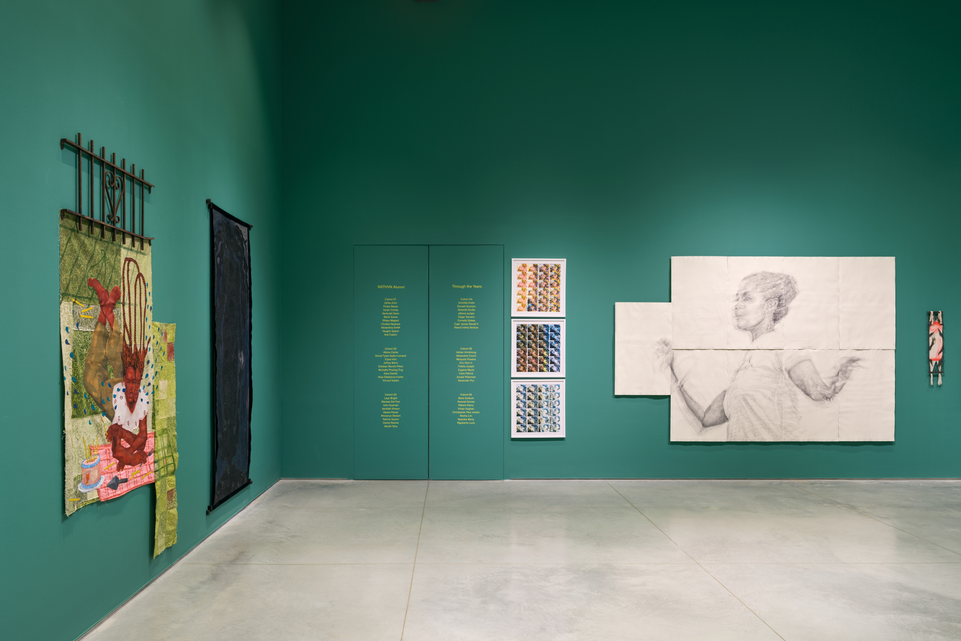 A corner of a gallery exhibition displaying various artworks and yellow vinyl text on the wall.
