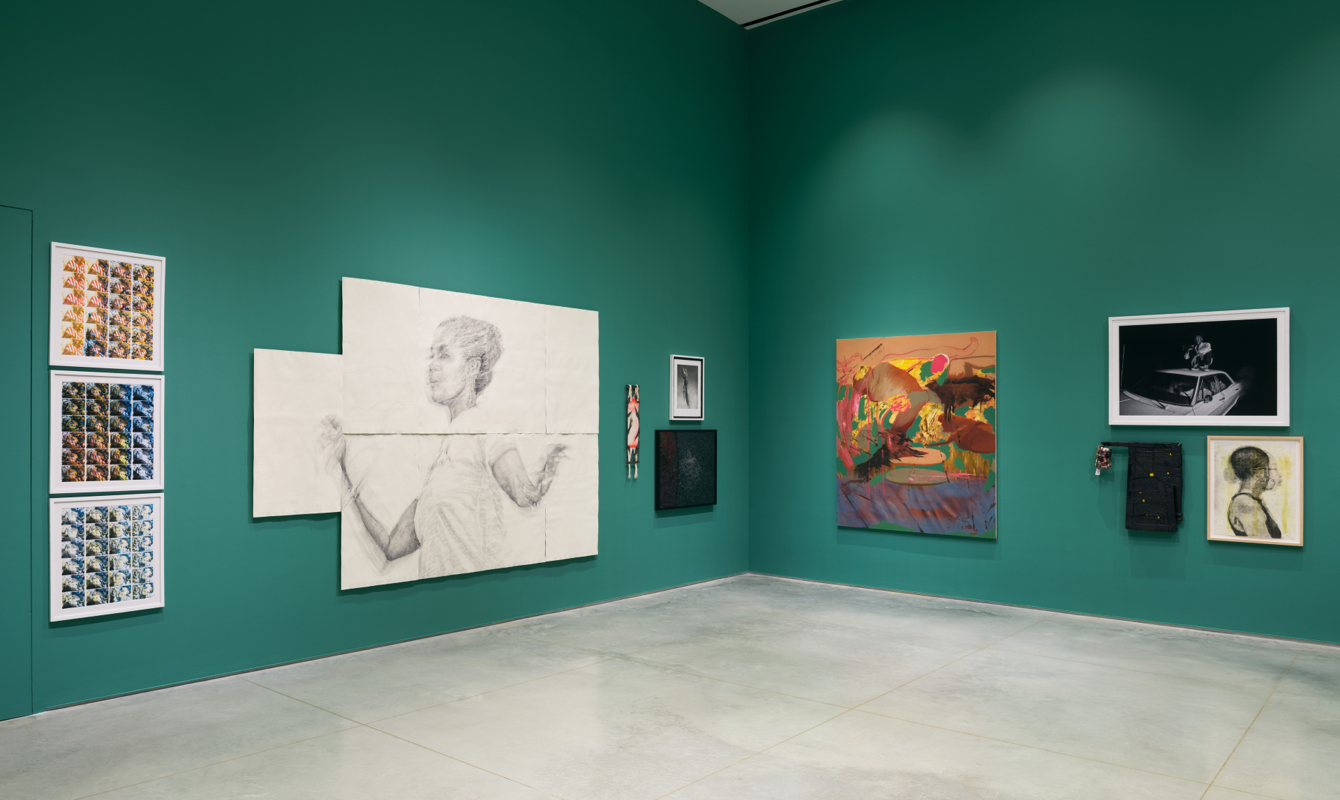 A corner of a gallery wall with hanging artworks that are framed and also of various mediums.