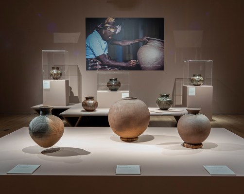 An exhibition display of various clay pots centering around an image of a Black woman carving into a pot.
