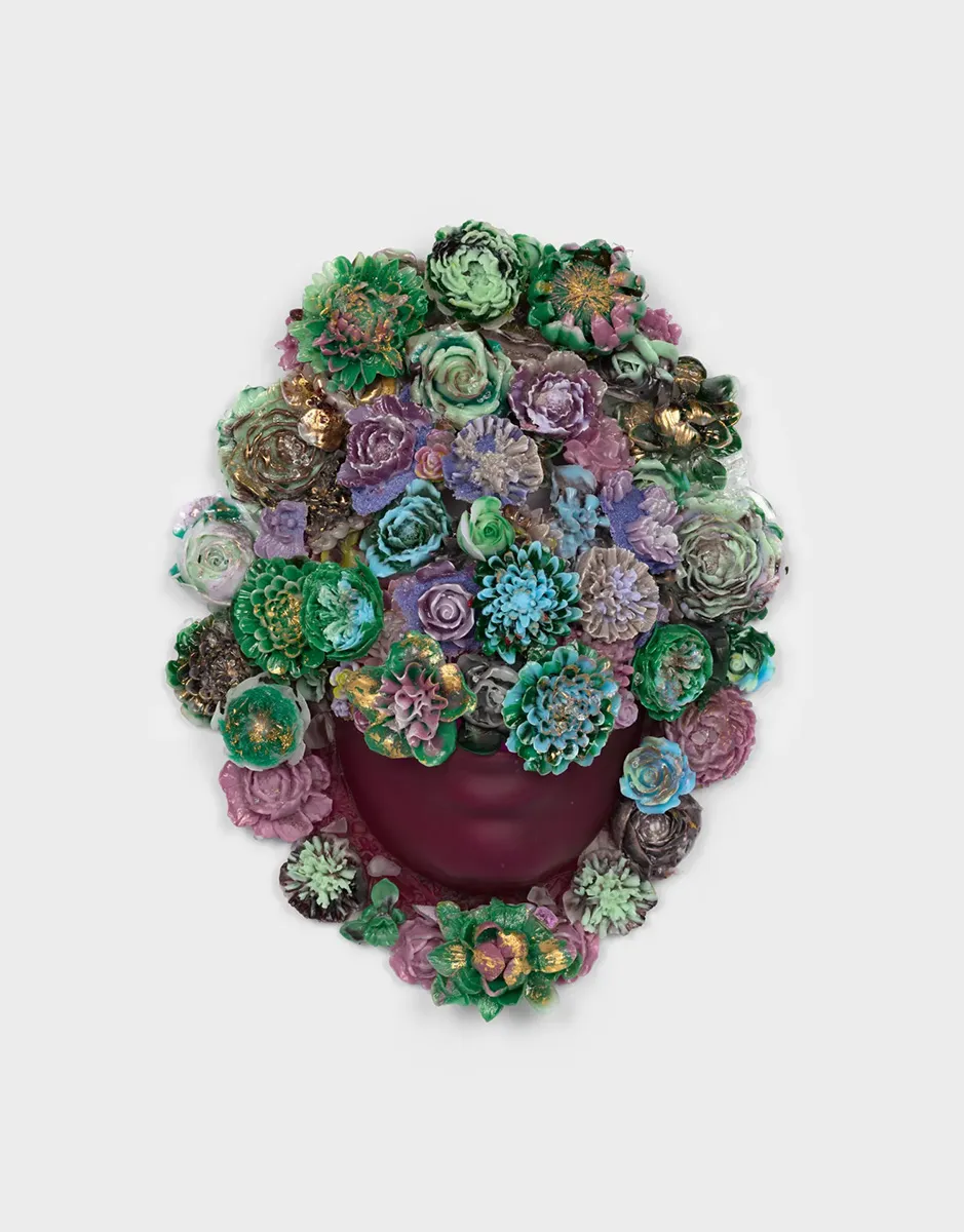 Glass mask of a face covered in flowers with only the mouth and chin exposed underneath.