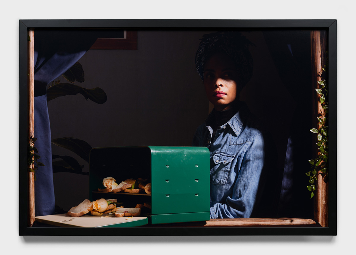 A framed photo of a Black woman sitting behind an open box with bread and roses spilling out of it.