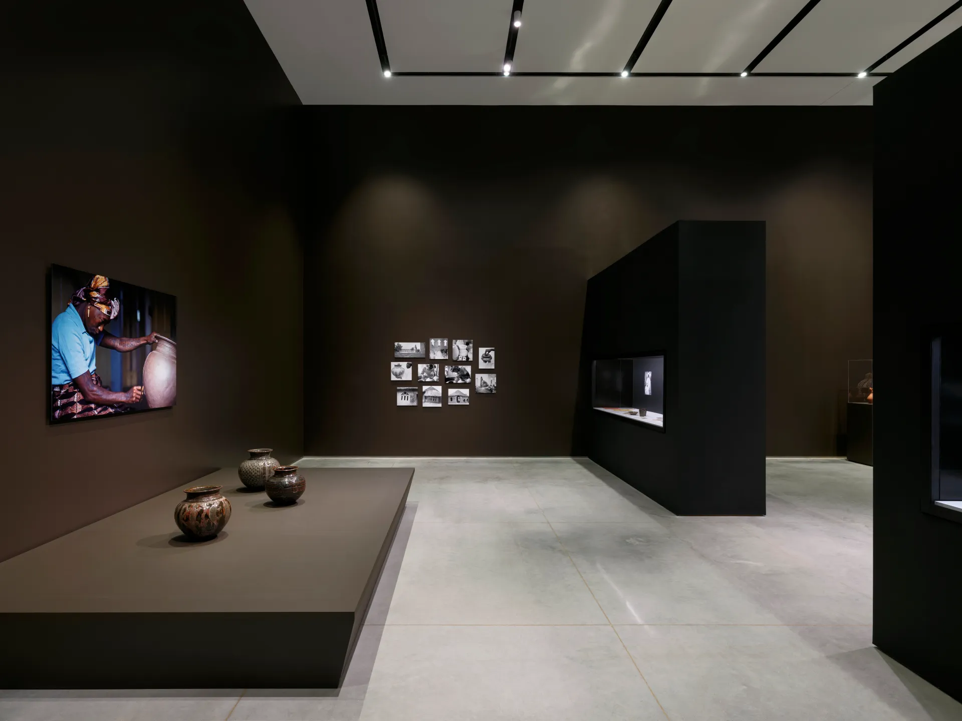 A gallery interior with photo prints on the walls, various ceramic pots, and architectural walls.