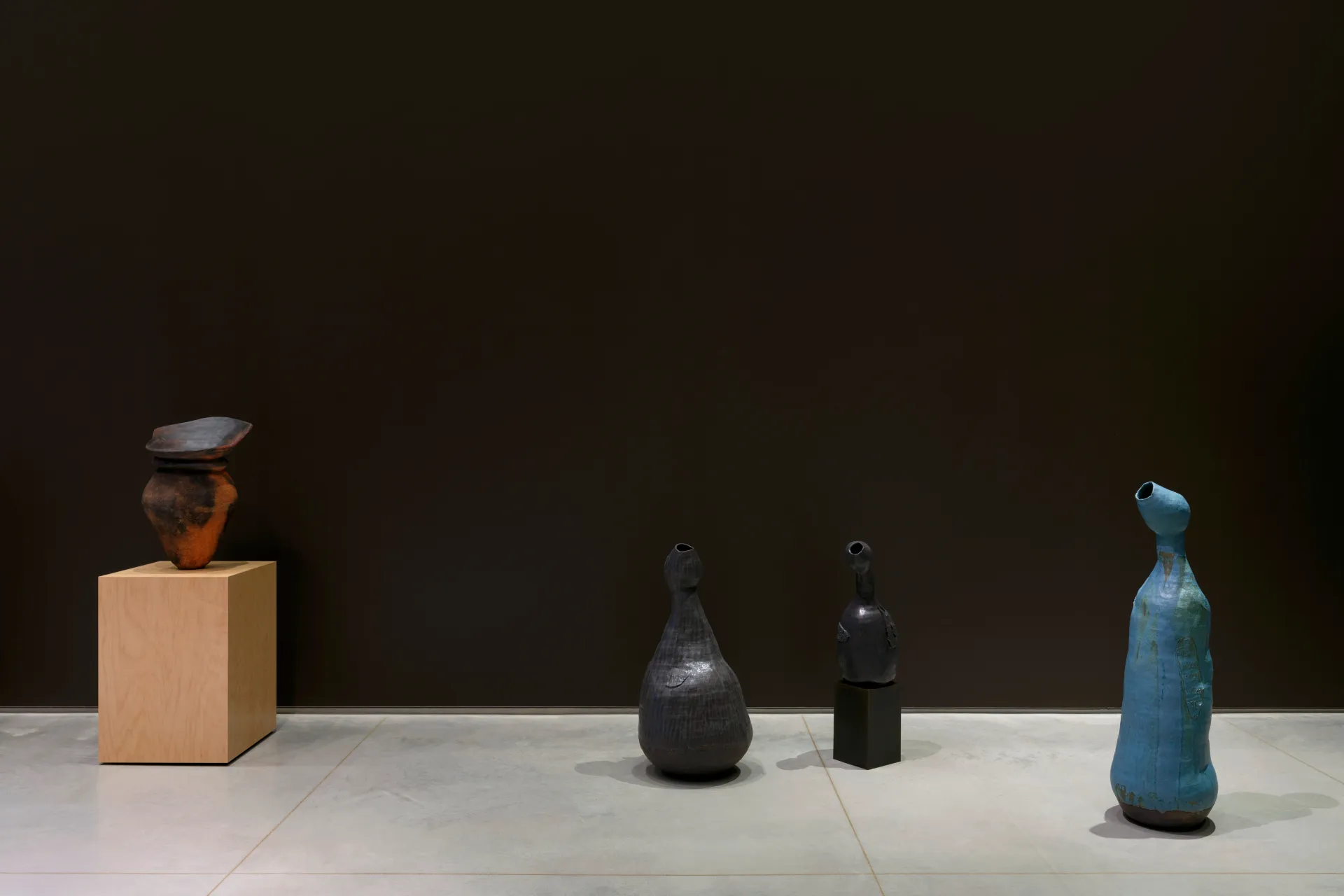 An exhibition showing a ceramic vase on a pedestal, and three clay sculptures with lumpy and irregular bodies.